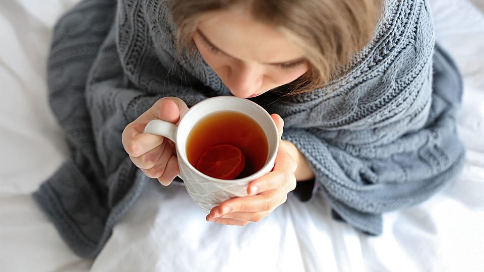 woman is wrapped in a thick scarf and drinking tea